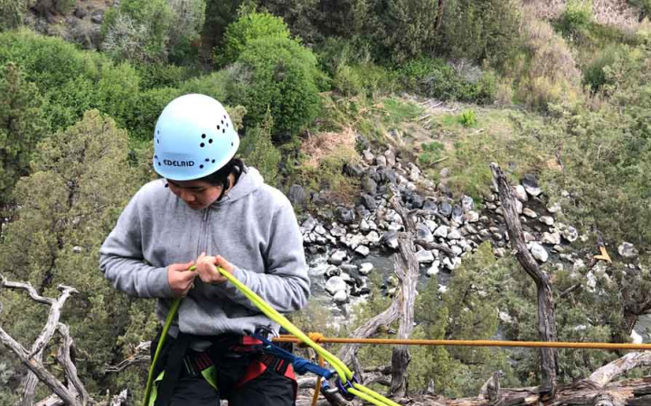woman ties rock climbing rope on course with outward bound